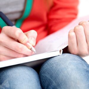 A person writing on paper with a pencil.