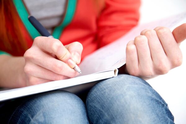 A person writing on paper with a pencil.