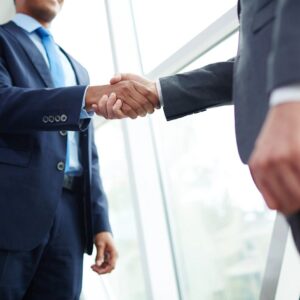 Two men in suits shaking hands over a window.