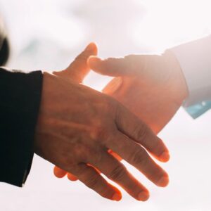 Two people shaking hands in front of a bright sun.