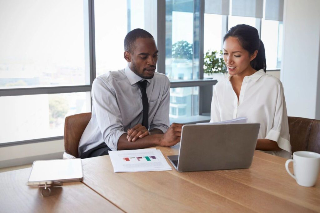 Two people sitting at a table looking at a laptop.