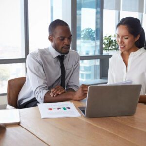 Two people sitting at a table looking at a laptop.